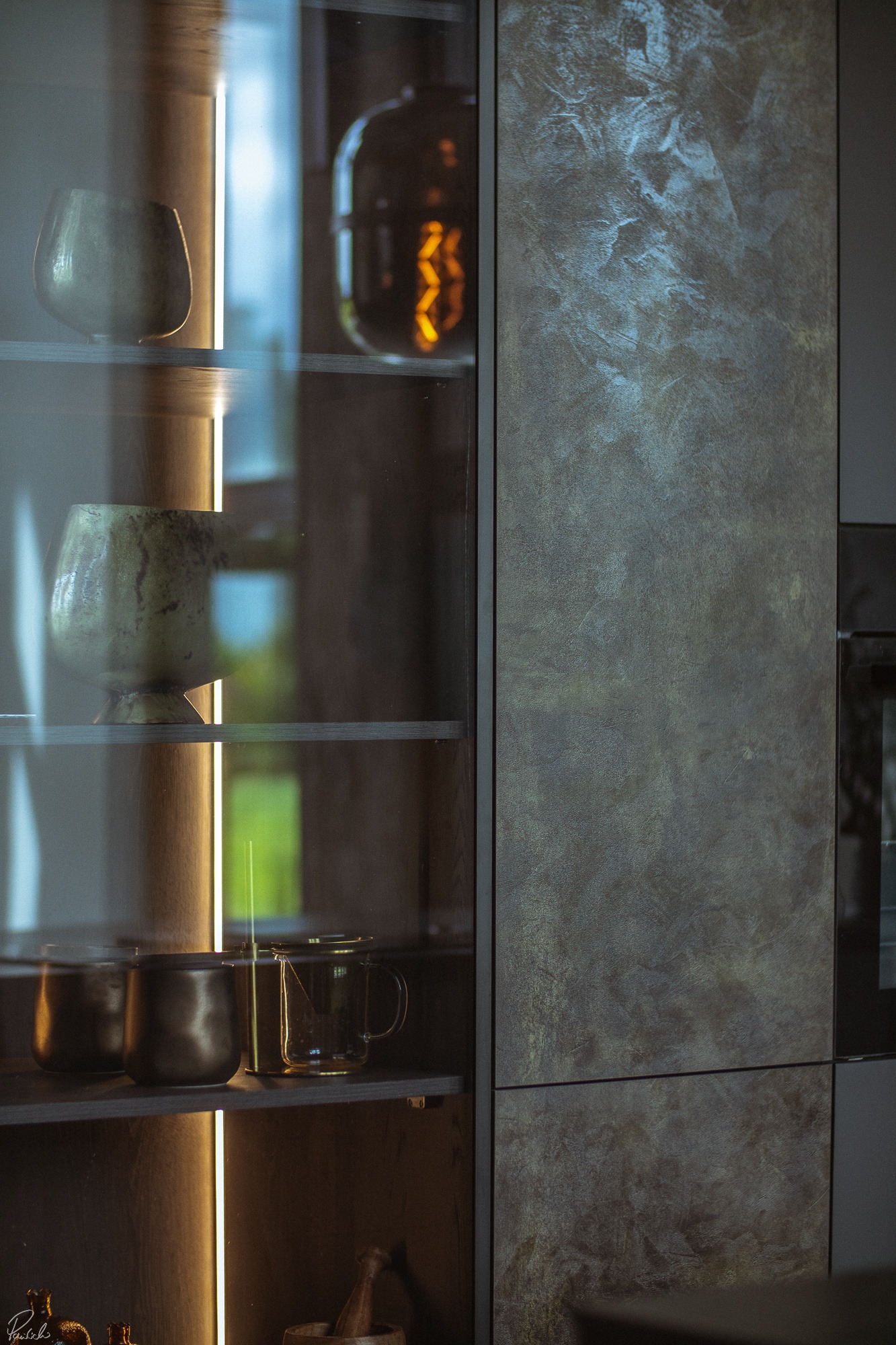 Nowoczesna szafka z podświetlanymi półkami prezentująca dekoracyjne naczynia i akcesoria kuchenne, z bliska widoczna struktura frontów.