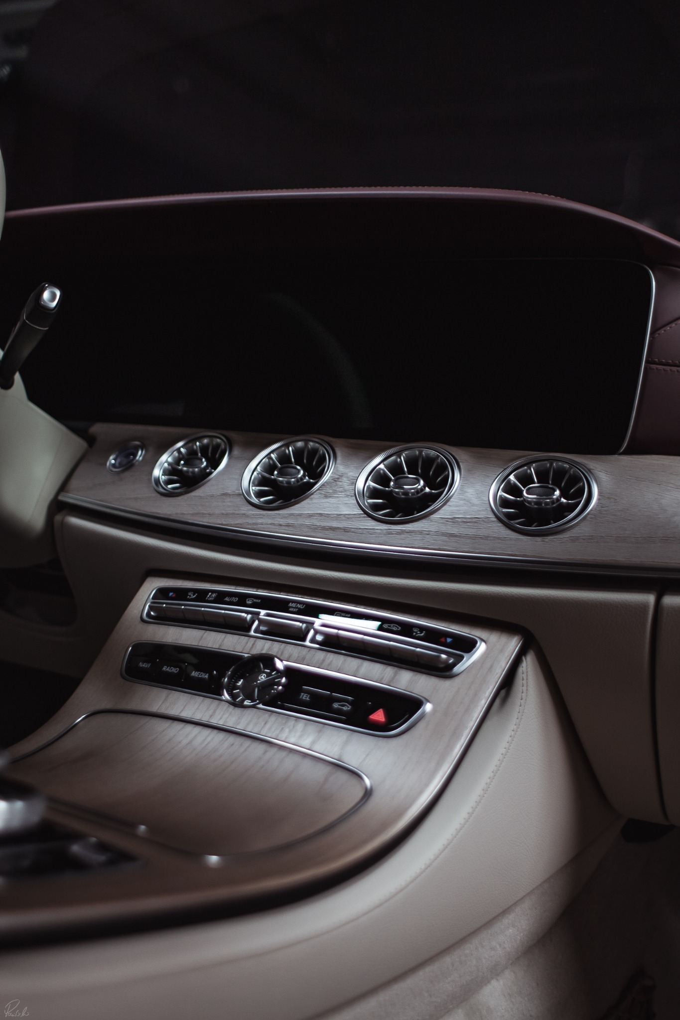 Wnętrze samochodu z drewnianym wykończeniem deski rozdzielczej, widoczne okrągłe kratki nawiewów i panel sterowania.