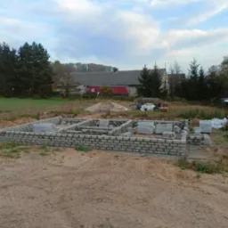 Wznoszenie fundamentów z bloczków betonowych w Ząbkowicach Śląskich, widoczne palety z bloczkami i przygotowany teren pod budowę domu.