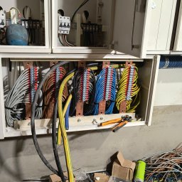 ELEKTRA Dariusz Glazer - Rozdzielnica elektryczna z uporządkowanymi przewodami w różnych kolorach, widoczne listwy zaciskowe, narzędzia do obróbki kabli i fragment ściany w tle.