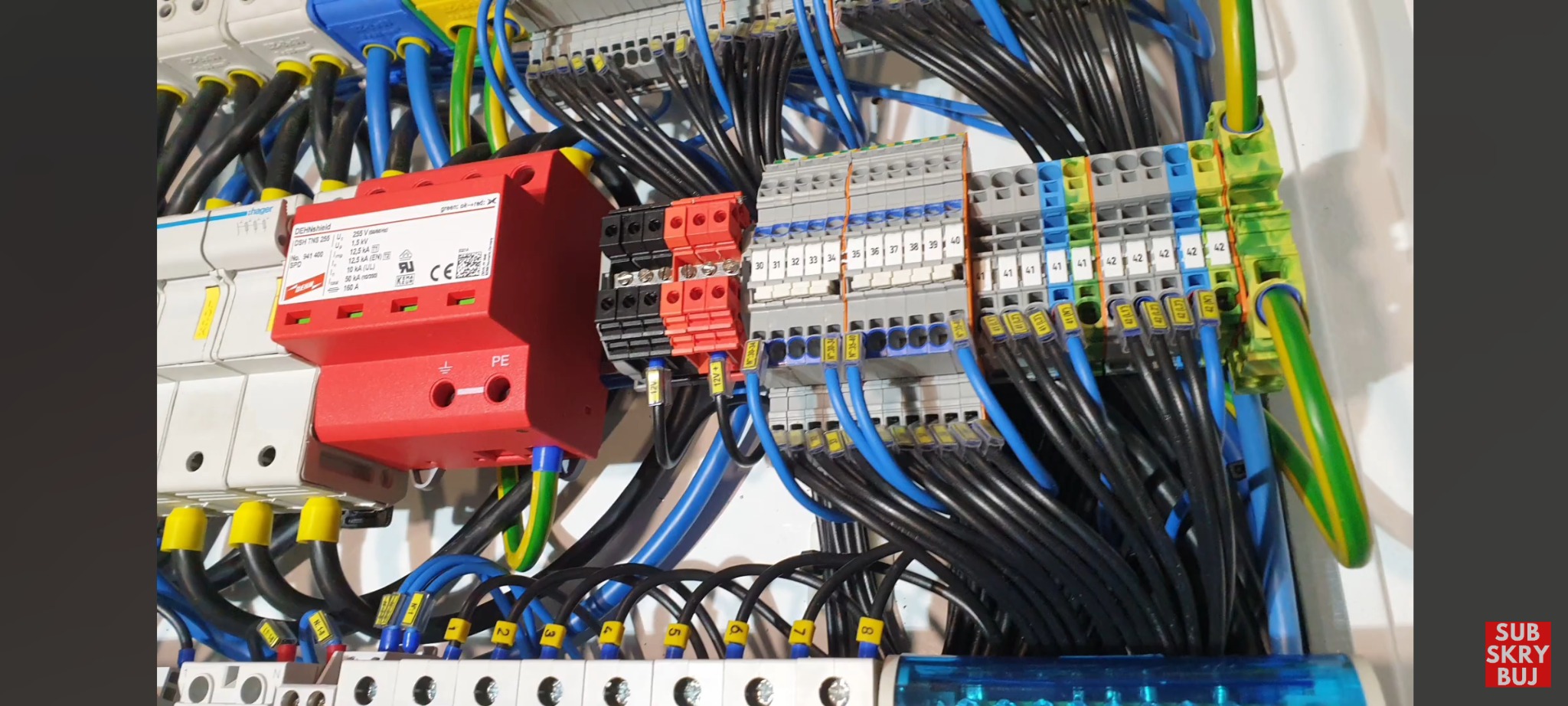 Szczegółowe ujęcie rozdzielnicy elektrycznej z widocznymi zabezpieczeniami przepięciowymi Dehn, listwami zaciskowymi i uporządkowanymi przewodami oznaczonymi numerami.