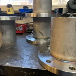 Spawane rury ze stali nierdzewnej z kołnierzami na warsztatowym stole, widoczne ślady obróbki i opalizujące spoiny.