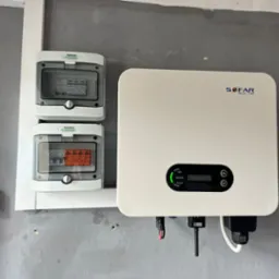 Zamontowany inwerter Sofar Solar z dwoma zabezpieczeniami NOARK w białych obudowach na szarej, surowej ścianie, widoczne diody sygnalizacyjne i podłączenia kablowe.