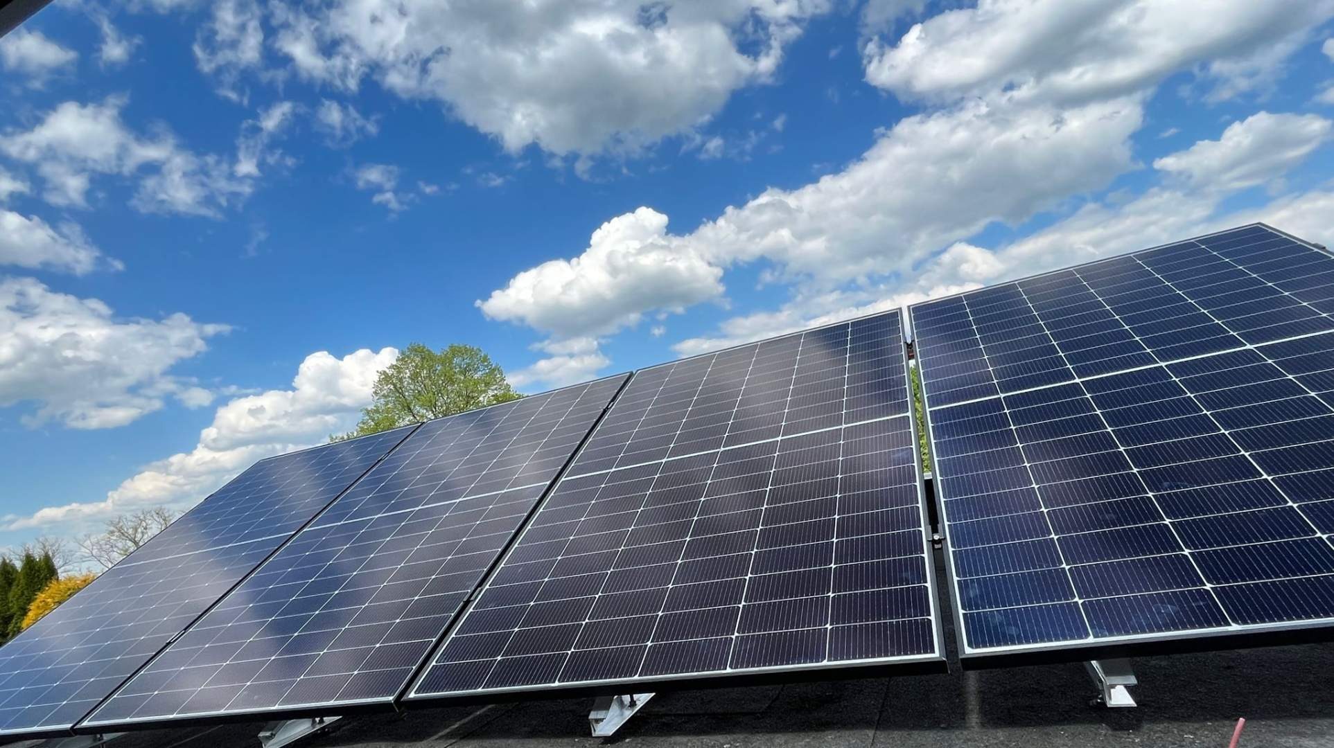 Instalacja paneli słonecznych w Śremie na tle błękitnego nieba z obłokami, widok z dołu ukazujący konstrukcję wsporczą.