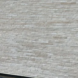 Elewacja budynku wykończona jasną, beżową cegłą klinkierową z wyraźną fugą. Widoczny fragment okna z lewej strony. Ujęcie z dołu ukazujące strukturę i kolorystykę elewacji.