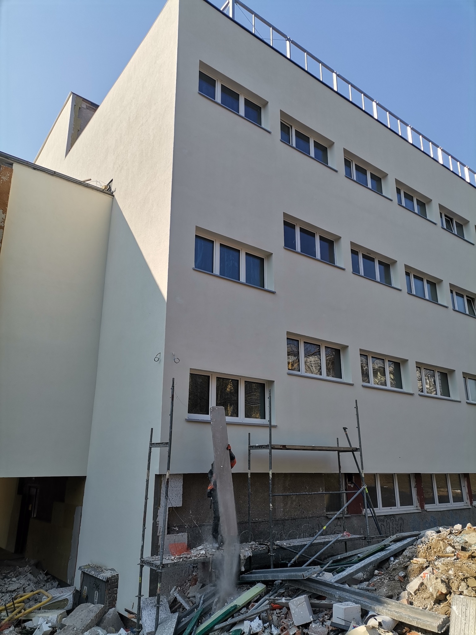 Budynek wielopiętrowy po remoncie elewacji, z widocznymi rusztowaniami i gruzem budowlanym u podstawy, sugerującymi trwające prace wykończeniowe.