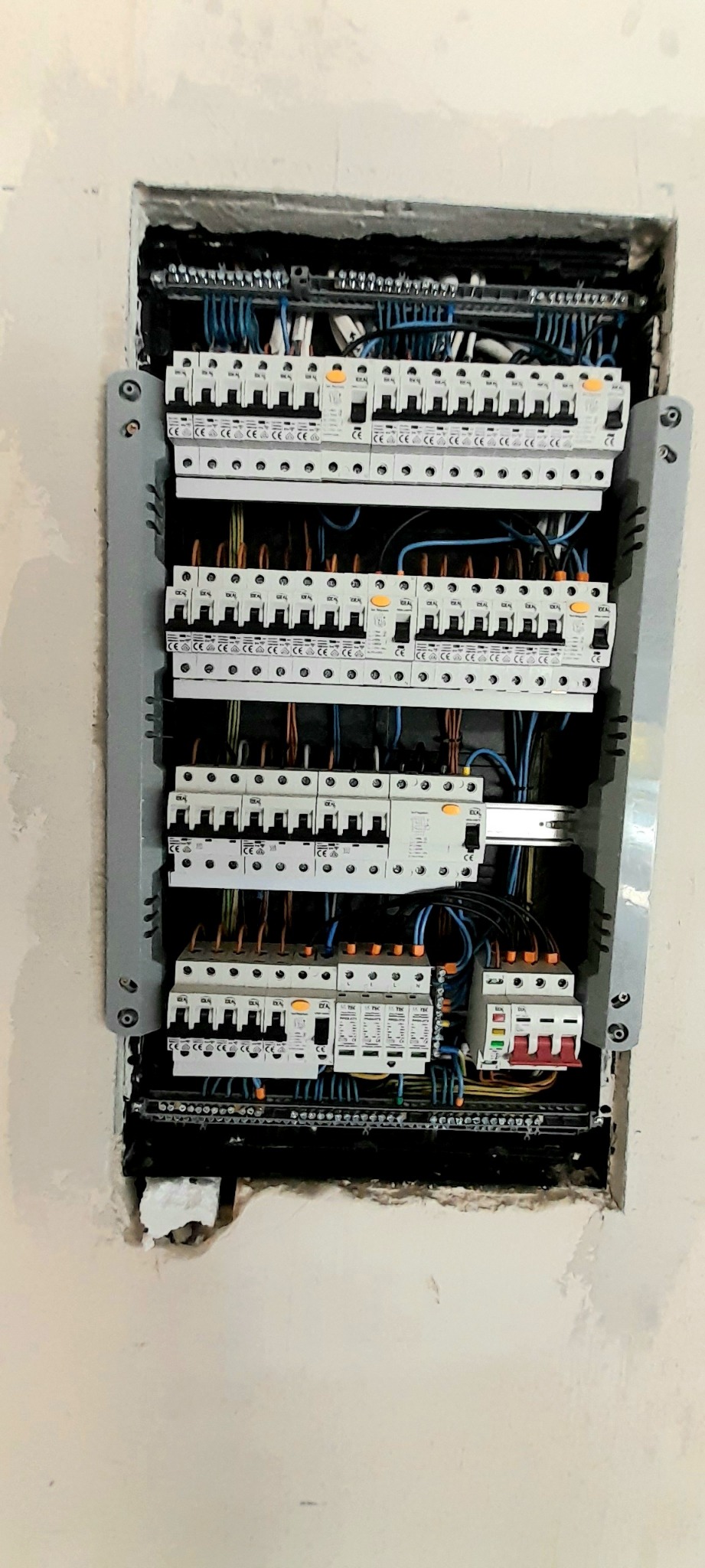 Rozdzielnica elektryczna z zamontowanymi bezpiecznikami i okablowaniem, osadzona we wnęce w ścianie, widoczne ślady po montażu.