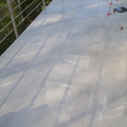 Usługi Budowlane - Świeżo ułożone, jasnoszare płytki na balkonie, widoczne narzędzia glazurnicze, wiadro i system poziomowania płytek.