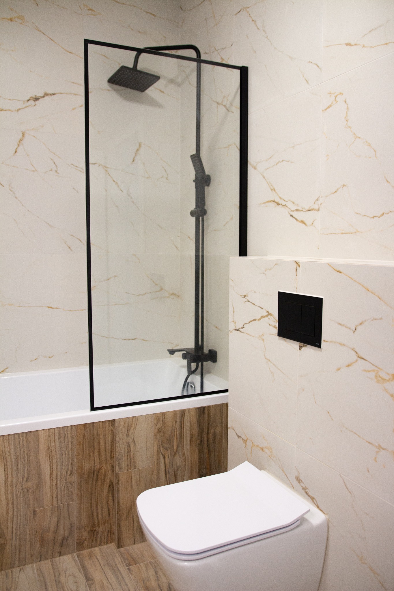 Nowoczesna łazienka z wanną i czarną armaturą, płytki imitujące marmur na ścianach, obudowa wanny z drewnopodobnych paneli, wisząca toaleta.