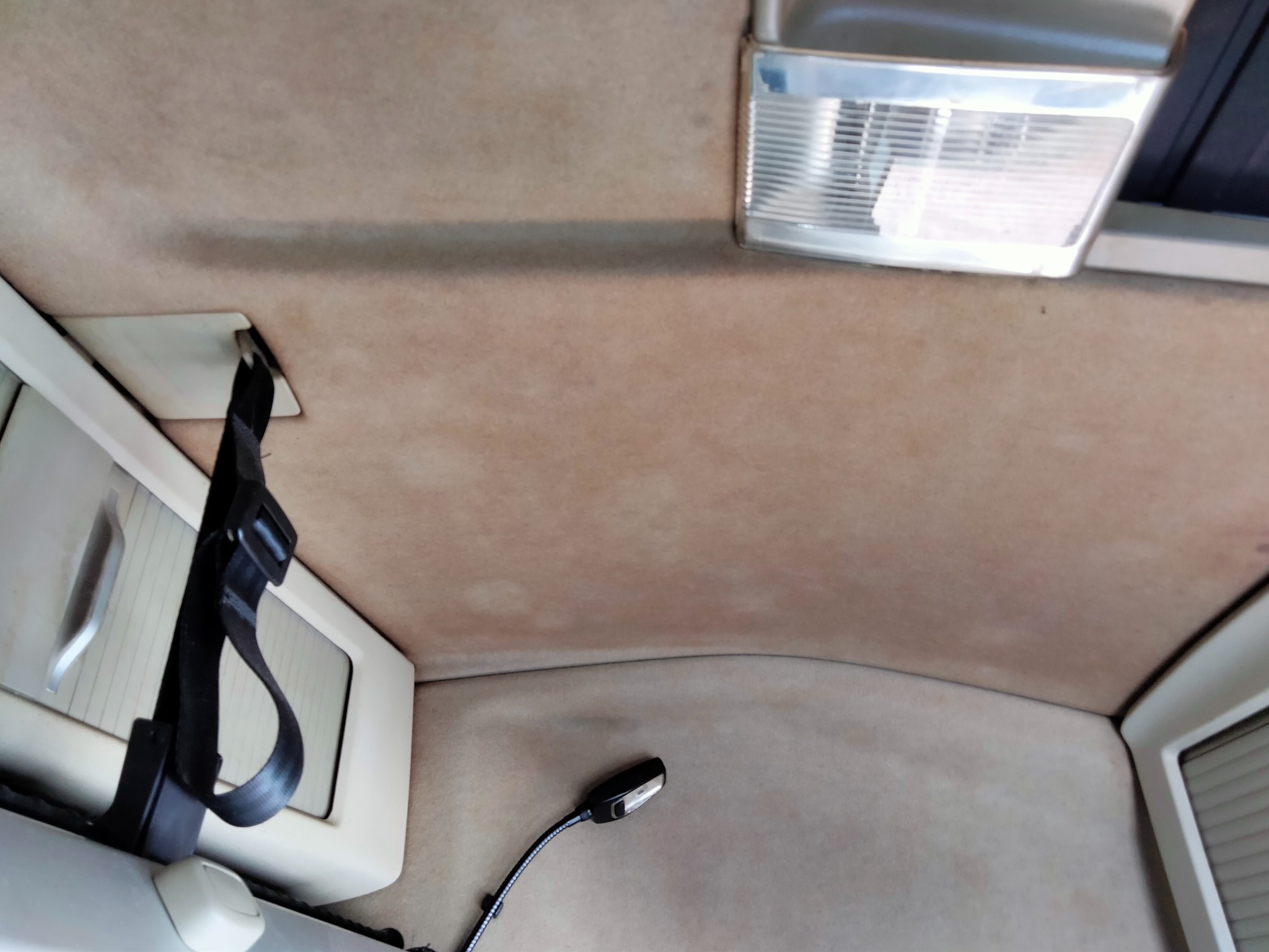 Wnętrze samochodu w Troszynie z beżową tapicerką sufitową, widoczna lampka, pas bezpieczeństwa i ślady użytkowania na materiale.