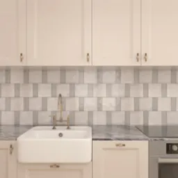 Kremowa zabudowa kuchenna z białym ceramicznym zlewem farmerskim, baterią w kolorze starego złota i marmurowym blatem, uzupełniona płytkami w odcieniach szarości.