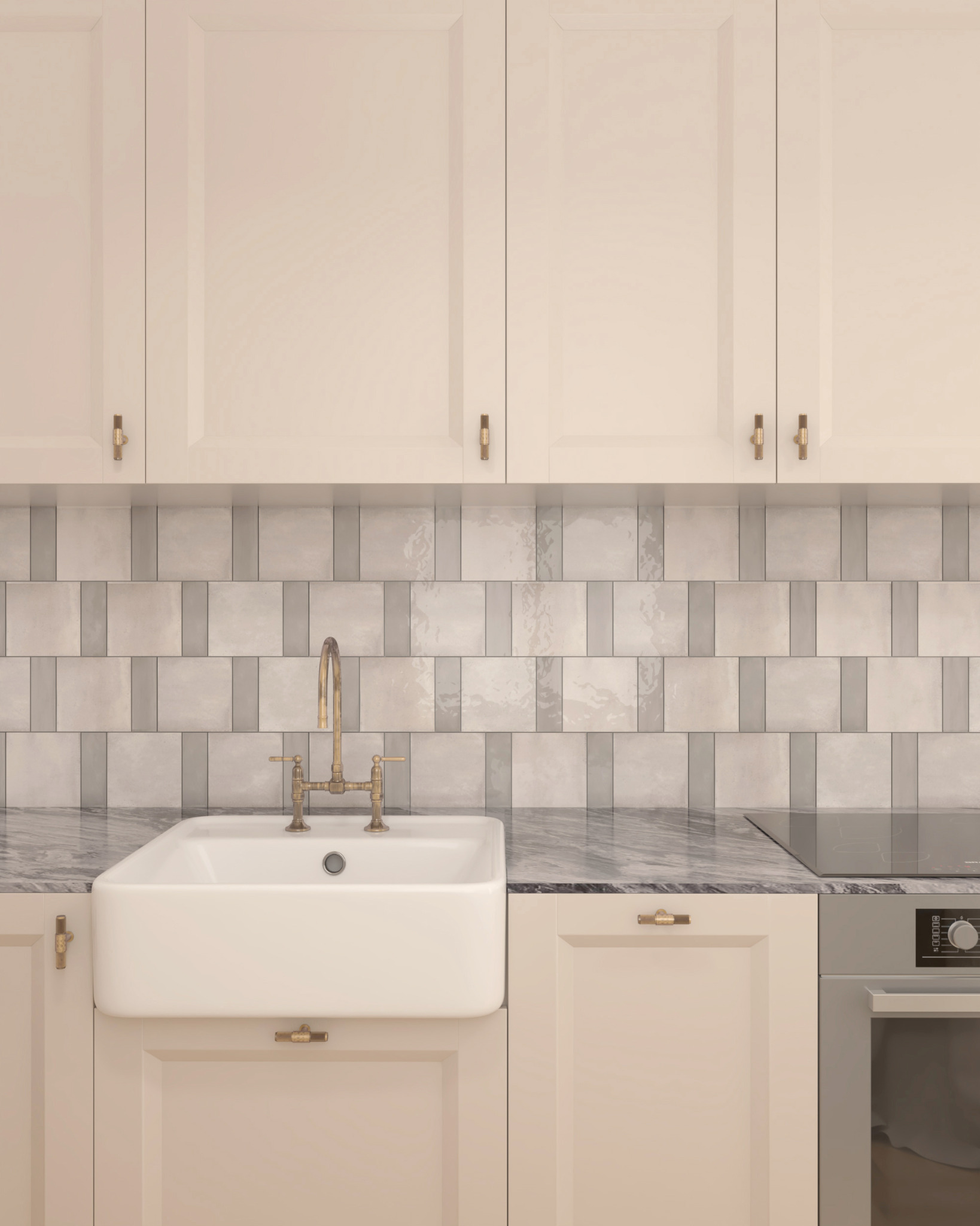 Kremowa zabudowa kuchenna z białym ceramicznym zlewem farmerskim, baterią w kolorze starego złota i marmurowym blatem, uzupełniona płytkami w odcieniach szarości.