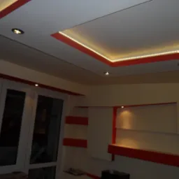 Sufit podwieszany z oświetleniem LED i halogenowym w odcieniach bieli i czerwieni, widoczne fragmenty ścian z półkami i oknem.