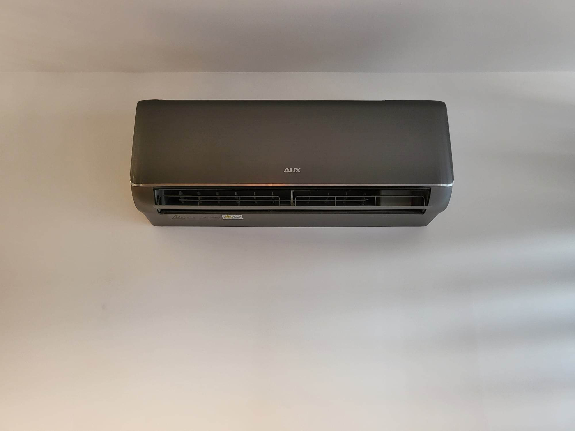 Szary klimatyzator AUX zamontowany na białej ścianie, widok z dołu, minimalistyczny design.