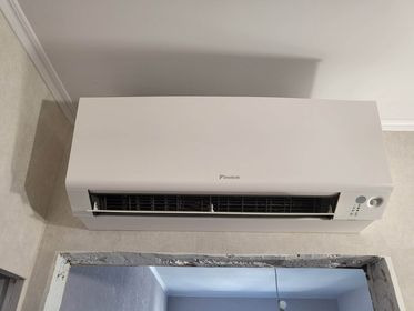 Klimatyzator ścienny marki Daikin zamontowany w pomieszczeniu, widoczny na tle surowej ściany i ramy okiennej w trakcie remontu.