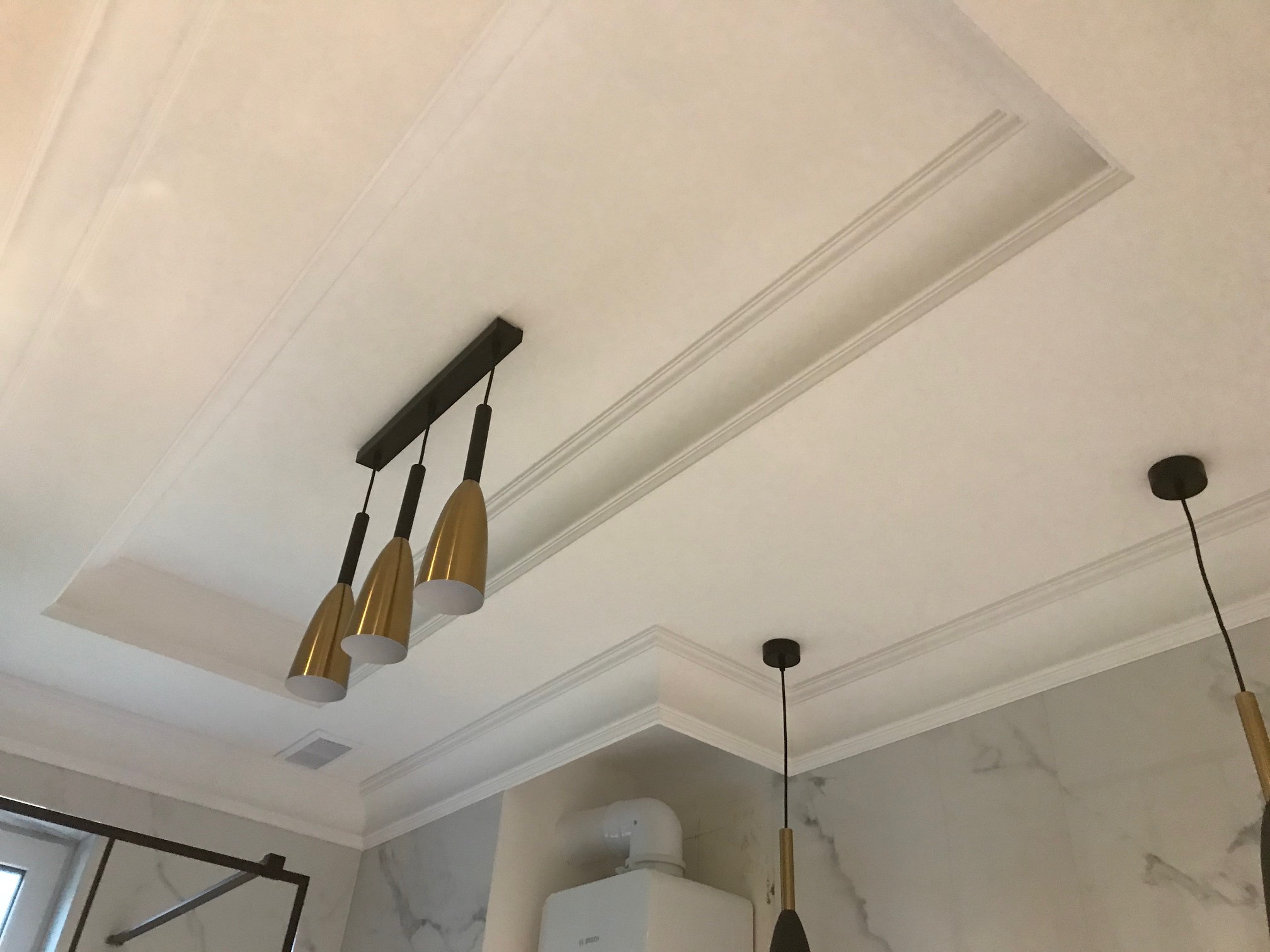 Dekoracyjny sufit podwieszany z oświetleniem punktowym i ozdobnymi listwami, widoczny fragment kotła gazowego na tle marmurowej ściany.