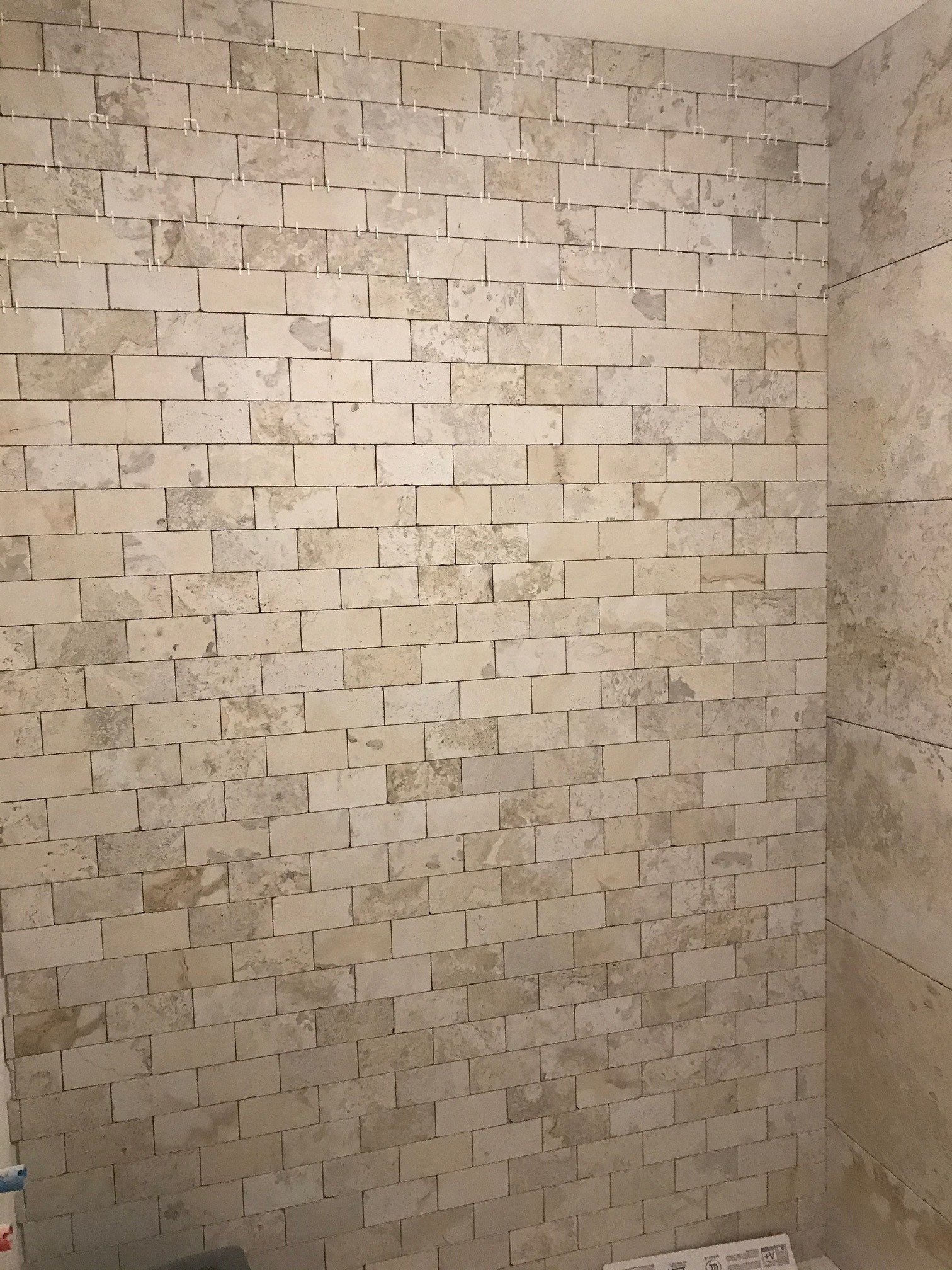 Układanie beżowych, prostokątnych płytek imitujących kamień na ścianie w Warszawie, widoczne krzyżyki dystansowe w spoinach.