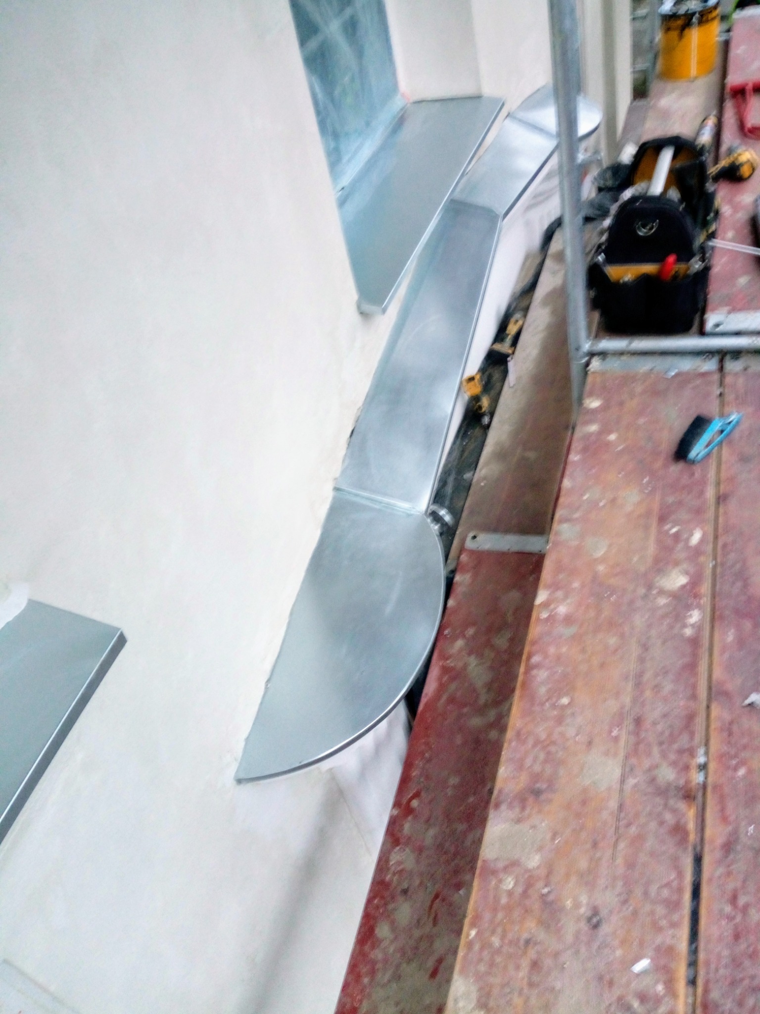 Montaż obróbek blacharskich z blachy ocynkowanej na ścianie budynku, widoczne narzędzia i rusztowanie.