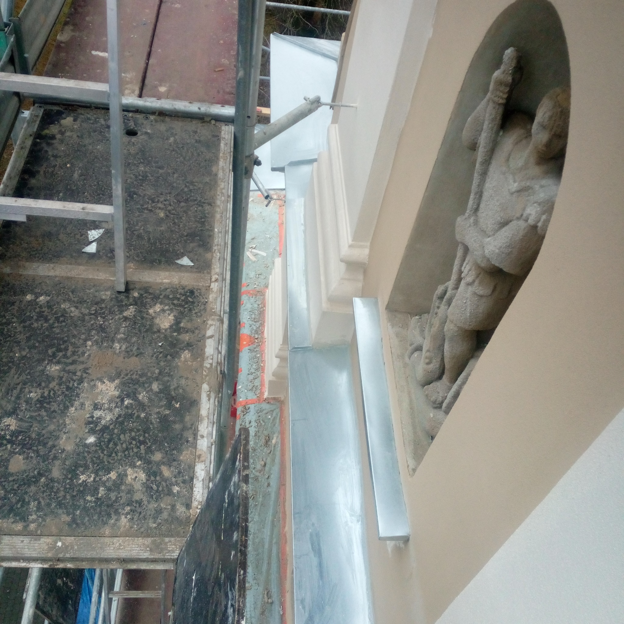 Renowacja elewacji budynku z dekoracyjną niszą i rzeźbą, widok z rusztowania, detale obróbek blacharskich.