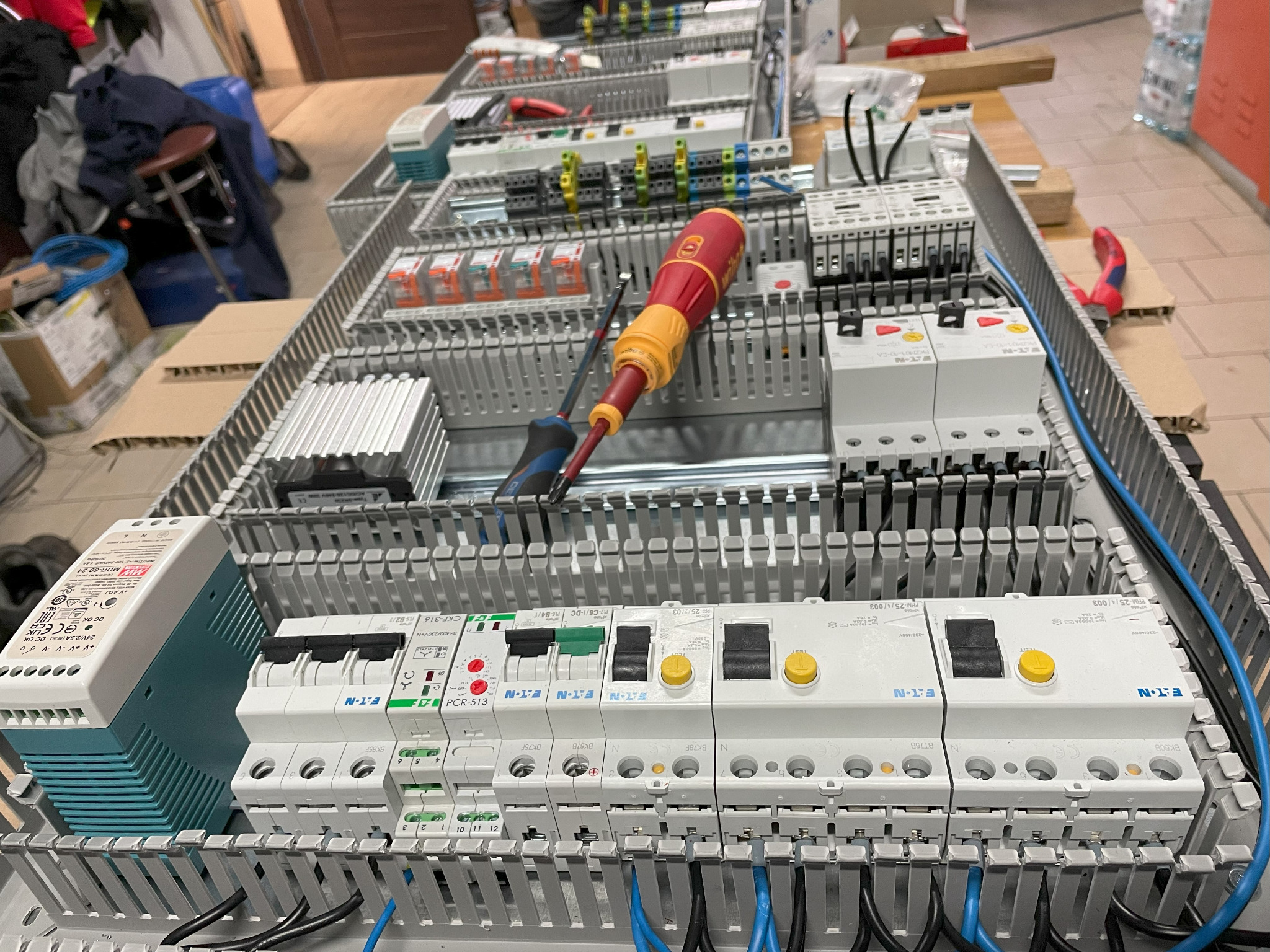 Rozdzielnica elektryczna w trakcie montażu, widoczne bezpieczniki, kable, listwy zaciskowe i dwa śrubokręty leżące na górze.