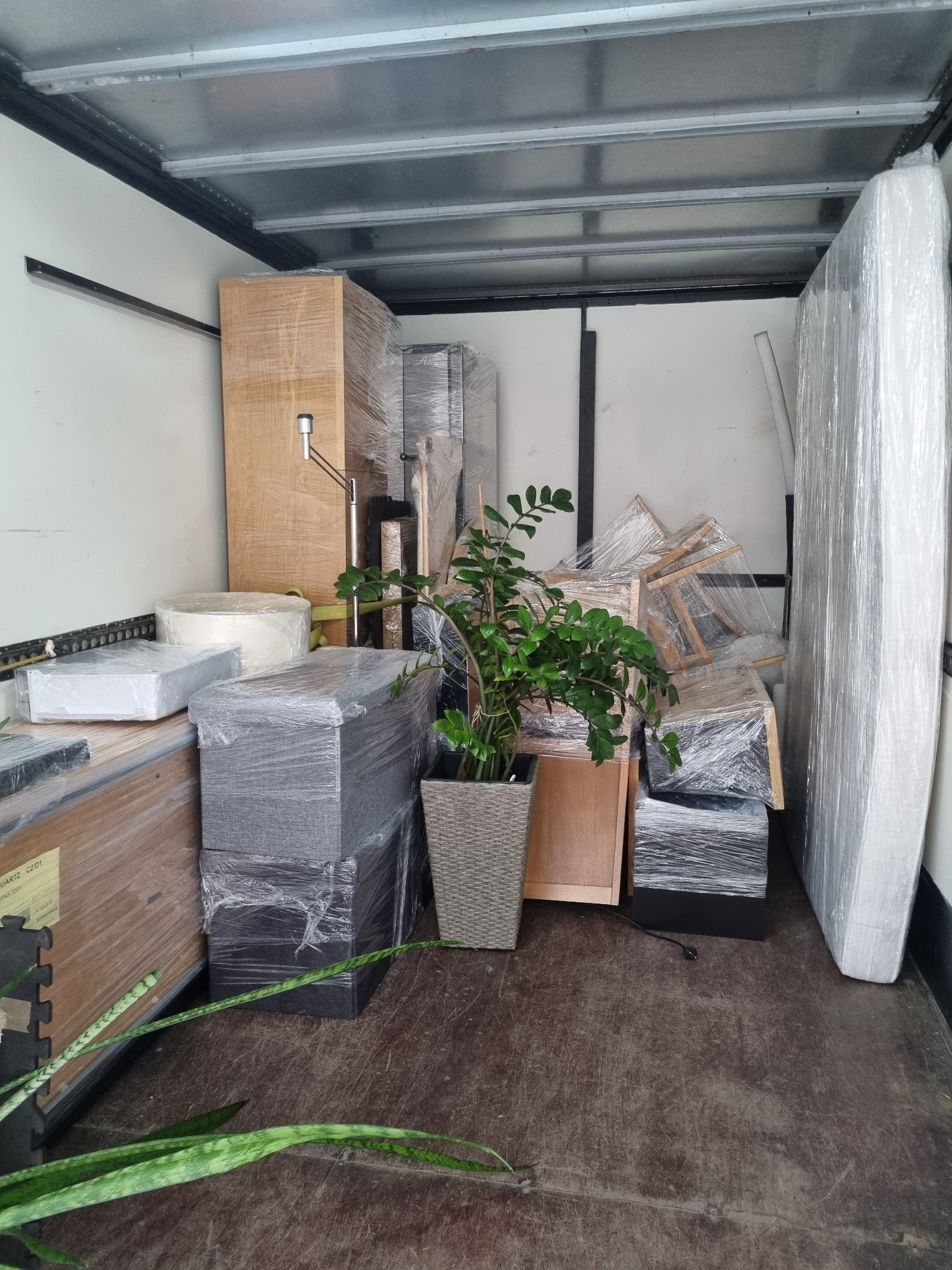 Wnętrze furgonetki wypełnione meblami i rośliną doniczkową zabezpieczonymi folią stretch przed transportem.