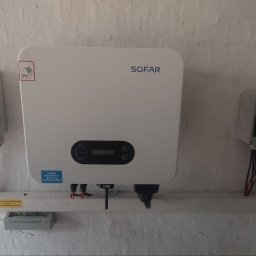Nasz Prąd S.A. - Zamontowany inwerter SOFAR z dwoma skrzynkami elektrycznymi na pomalowanej ścianie o nierównej fakturze, widoczne kable i naklejki ostrzegawcze.