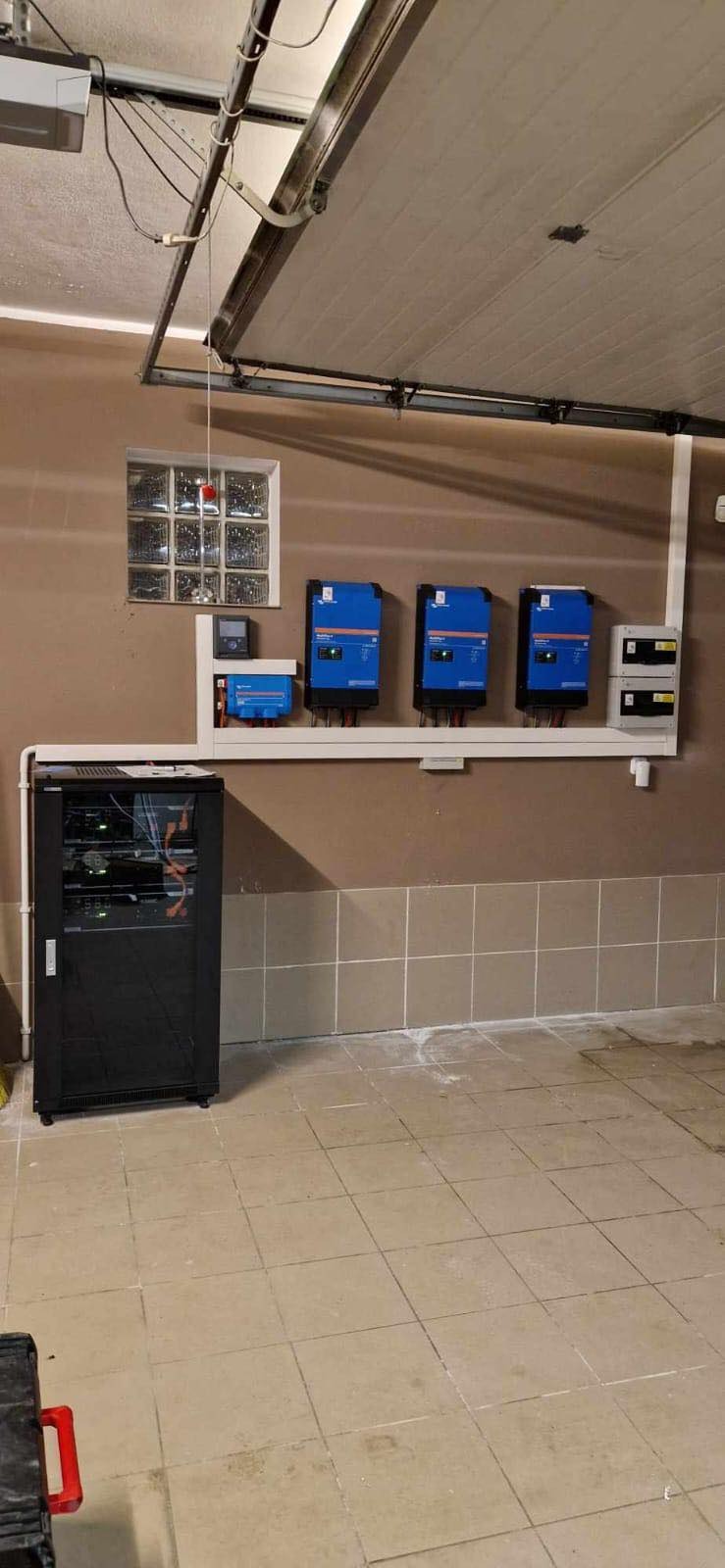 Instalacja falowników i okablowania w garażu, widoczna szafa rack z elektroniką po lewej stronie.