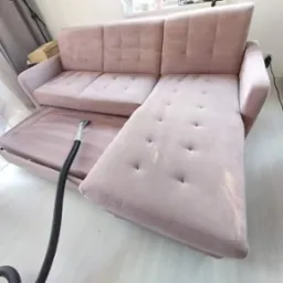 Jasnoróżowa kanapa narożna z wysuwanym siedziskiem czyszczona odkurzaczem piorącym, widoczne ślady wilgoci po czyszczeniu.