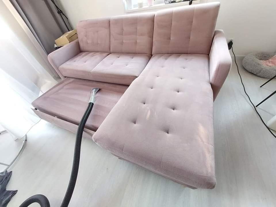 Jasnoróżowa kanapa narożna z wysuwanym siedziskiem czyszczona odkurzaczem piorącym, widoczne ślady wilgoci po czyszczeniu.