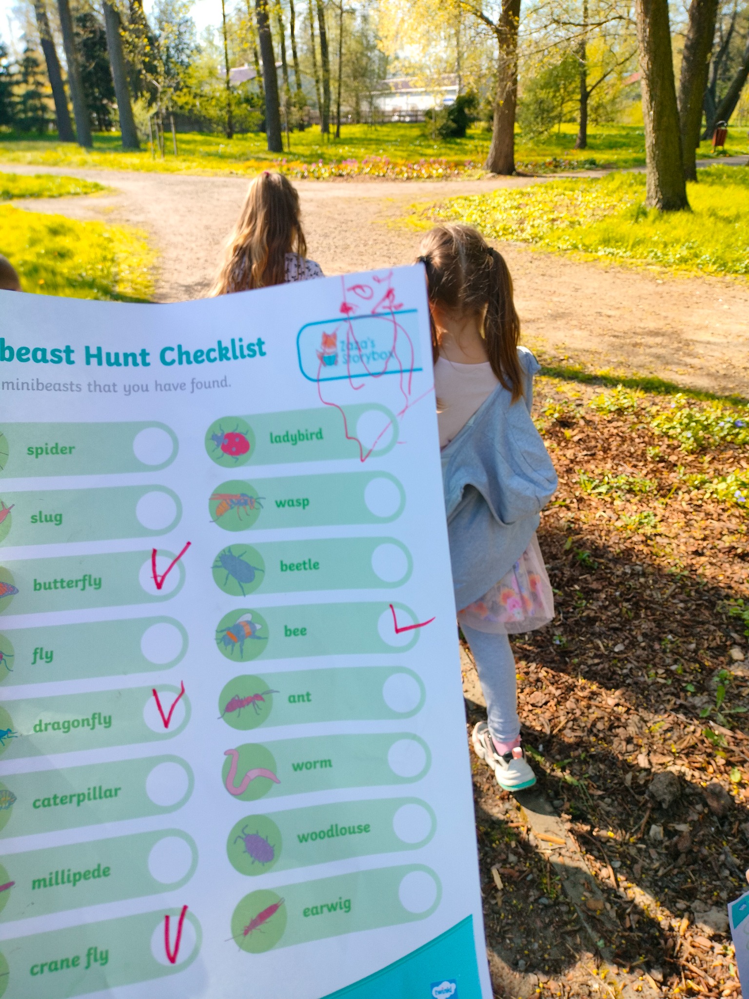 Dziewczynka z checklistą 'Beast Hunt' w parku, zaznaczone motyl, ważka i komarnica.