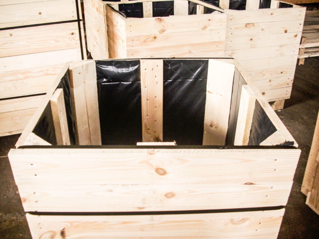 Surowe, drewniane skrzynie z czarną folią wewnątrz, ustawione jedna za drugą w magazynie.