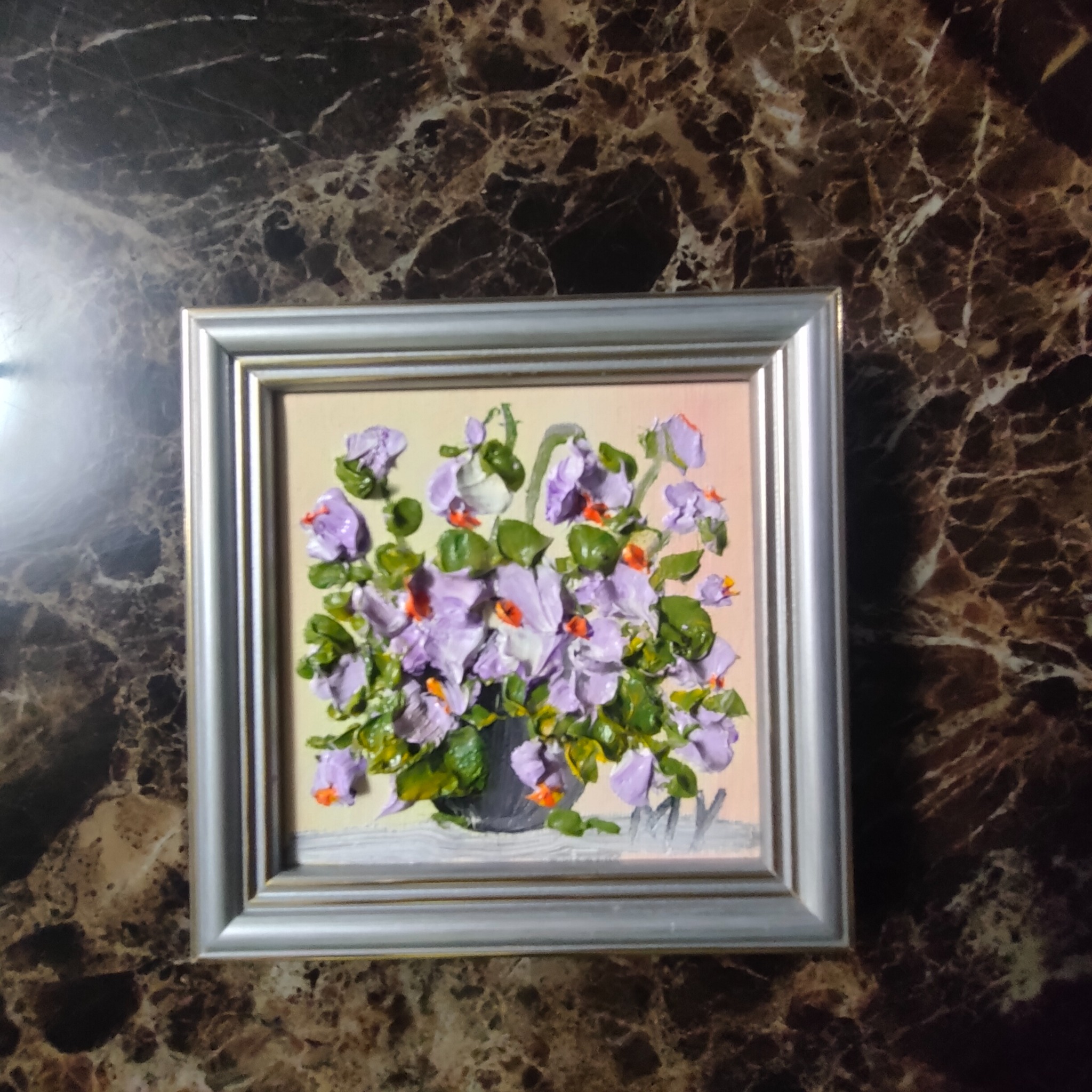 Obraz olejny przedstawiający bukiet fiołków w szarym wazonie, w srebrnej ramce, na marmurowym tle. Impastowa technika malarska z wyraźną fakturą farby.