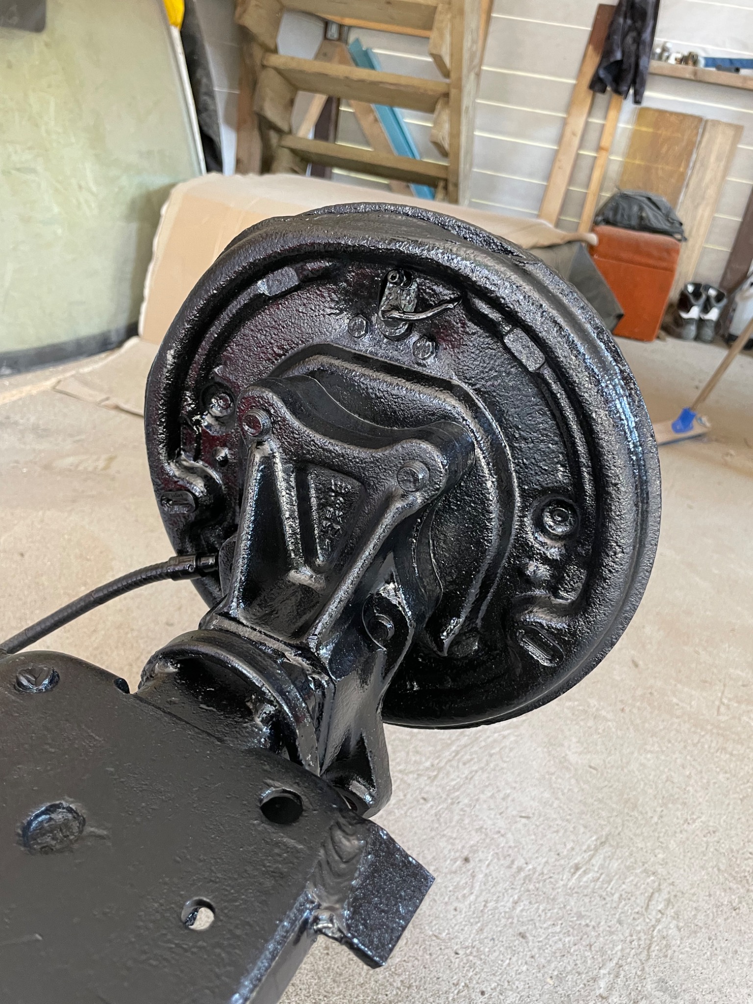 Pompa hamulcowa po renowacji, pokryta czarną, błyszczącą farbą, widoczna na tle warsztatu z drabiną i narzędziami.