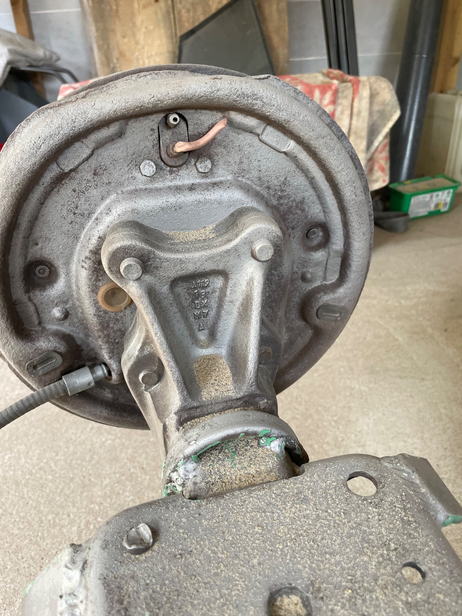 Szara, metalowa tarcza hamulcowa z widocznymi śladami korozji i spawania, zamontowana na osi, z przewodem hamulcowym podłączonym do boku, w tle widoczne przedmioty w warsztacie.