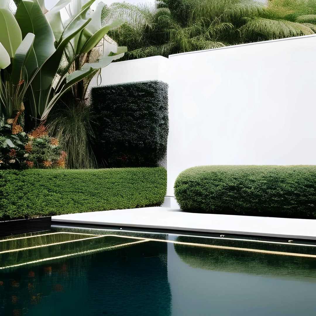 Minimalistyczny ogród z geometrycznie przyciętymi krzewami, białymi ścianami i ciemnym lustrem wody z ledowym oświetleniem.
