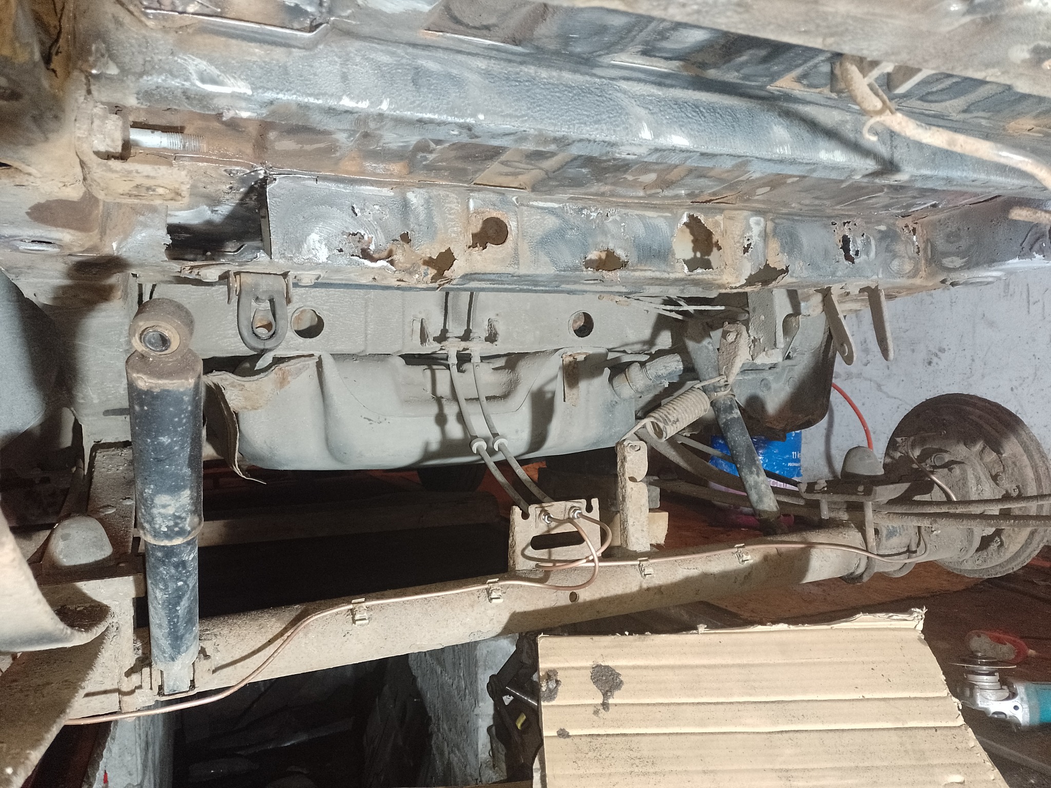 Widok od dołu na skorodowane podwozie samochodu w trakcie naprawy, widoczne dziury korozyjne i elementy zawieszenia.