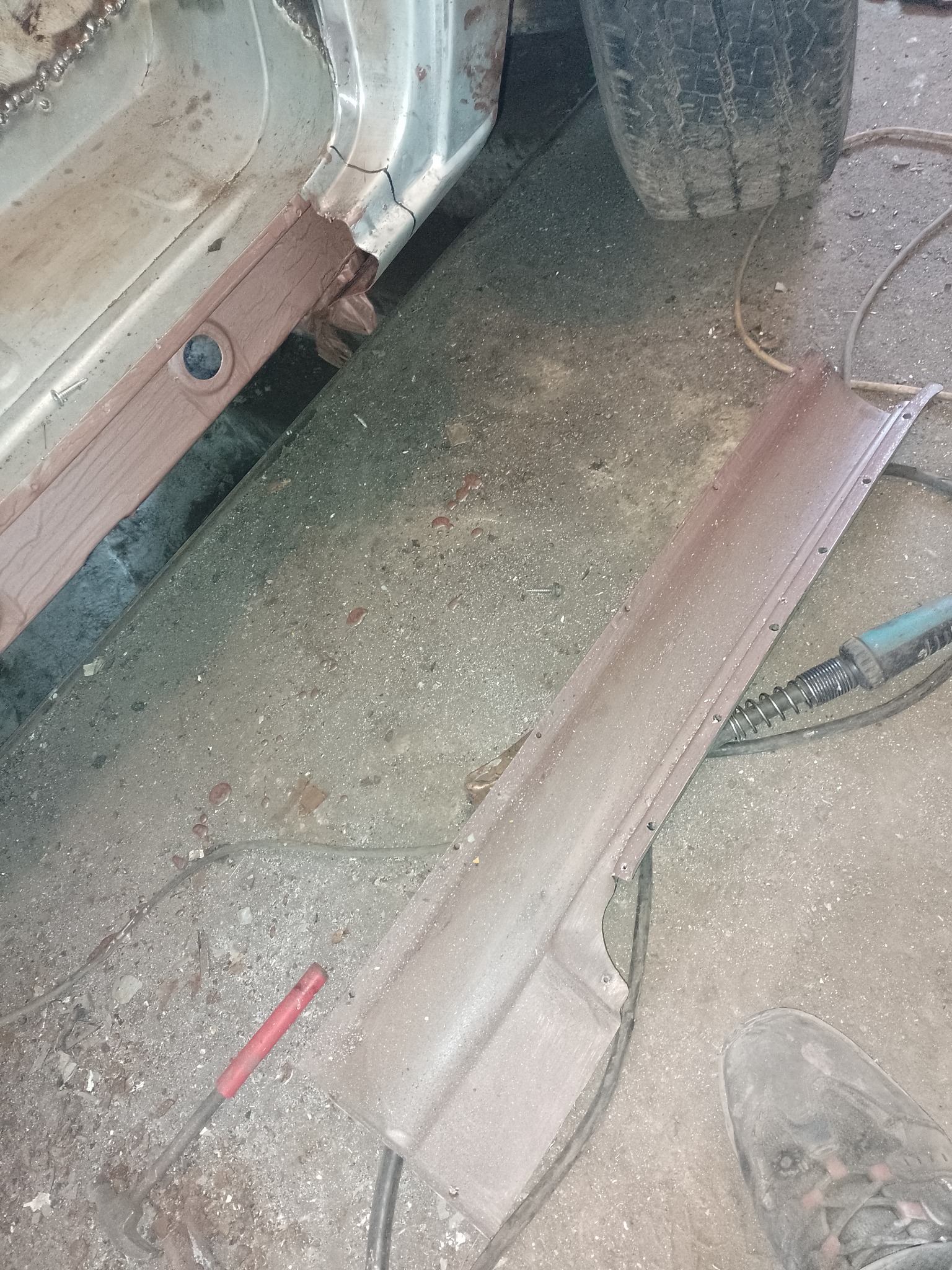 Wymiana progu w samochodzie w warsztacie w Sierakowicach, widoczny fragment karoserii i nowy element progu przygotowany do montażu, narzędzia leżące na podłodze.