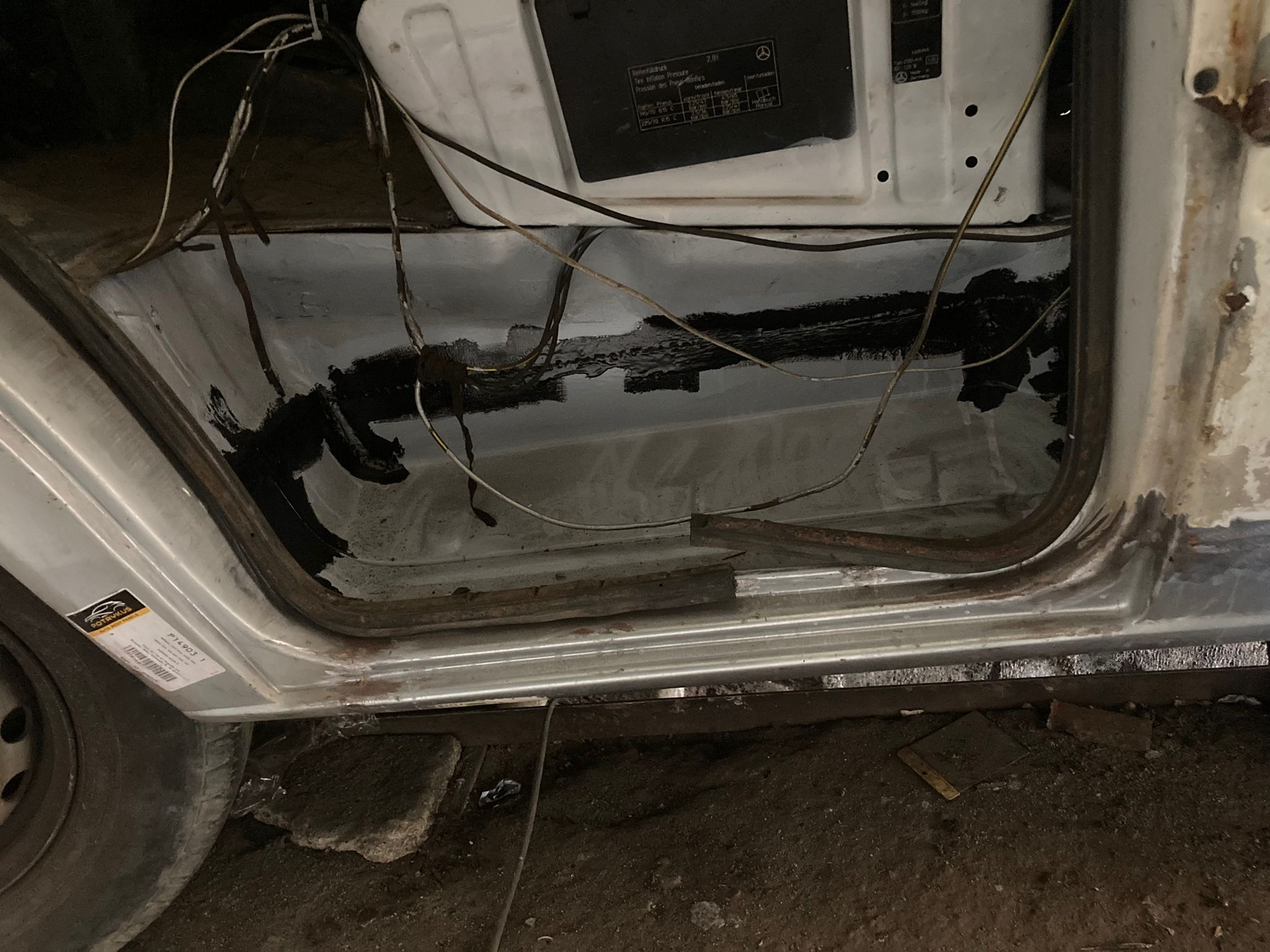 Wnętrze progu samochodu marki Mercedes po nałożeniu czarnej powłoki antykorozyjnej, widoczne przewody i naklejka z informacjami o ciśnieniu w oponach.