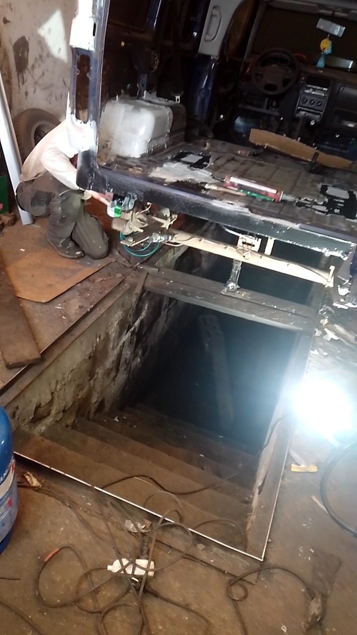 Demontaż podwozia samochodu w warsztacie, widoczny fragment podłogi i schody do piwnicy w tle.