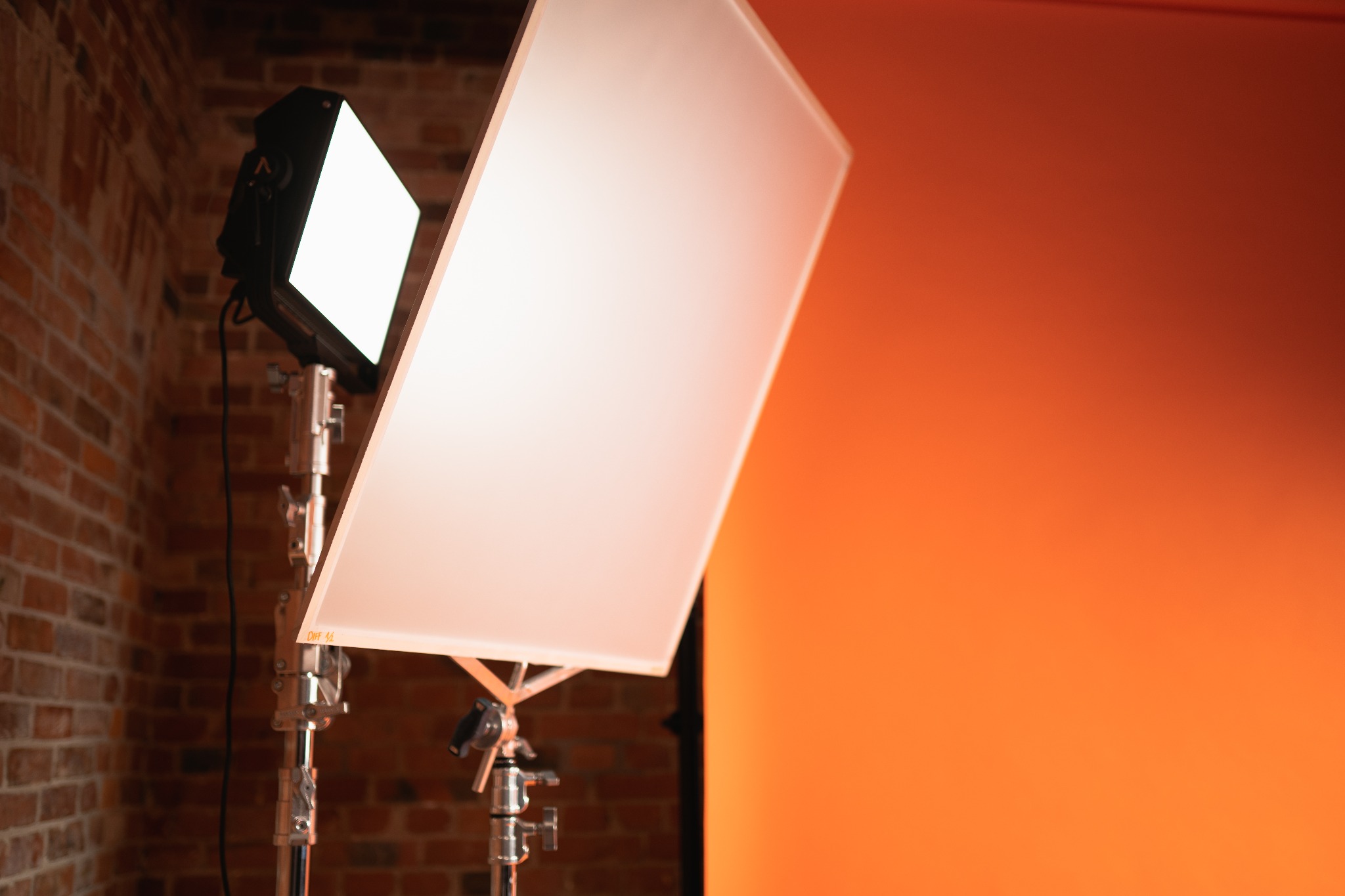 Studio lighting setup featuring a softbox on a stand, positioned against a brick wall and an orange backdrop.