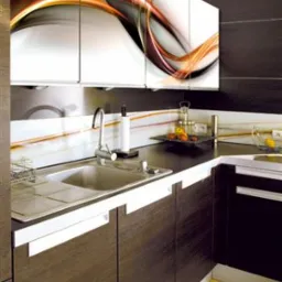 Ciemnobrązowe szafki kuchenne z białymi uchwytami i górnymi szafkami z abstrakcyjnym wzorem w kolorach pomarańczowym, szarym i białym, widok na zlew i blat.