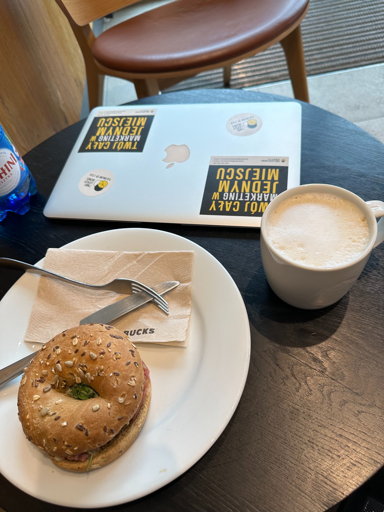 Laptop z naklejkami marketingowymi na stoliku kawiarnianym obok kawy i bajgla. Przerwa w pracy, spotkanie biznesowe w kawiarni.