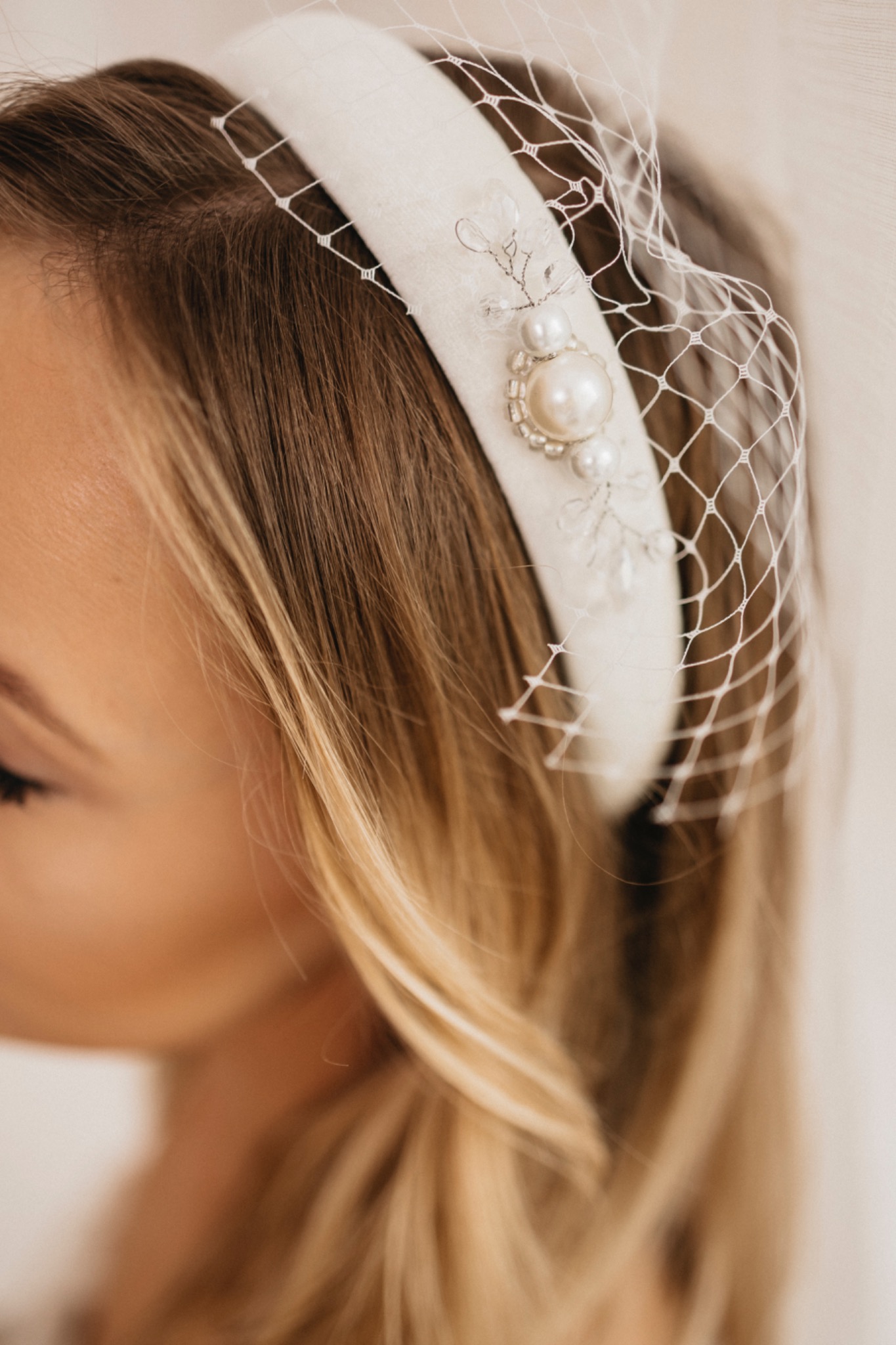 Blond włosy kobiety z białą opaską ozdobioną perłami i siateczką.