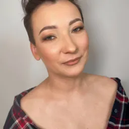 Portret kobiety z krótkimi włosami, subtelnym makijażem oczu i ust w odcieniach nude, ubrana w koszulę w czerwoną kratę.