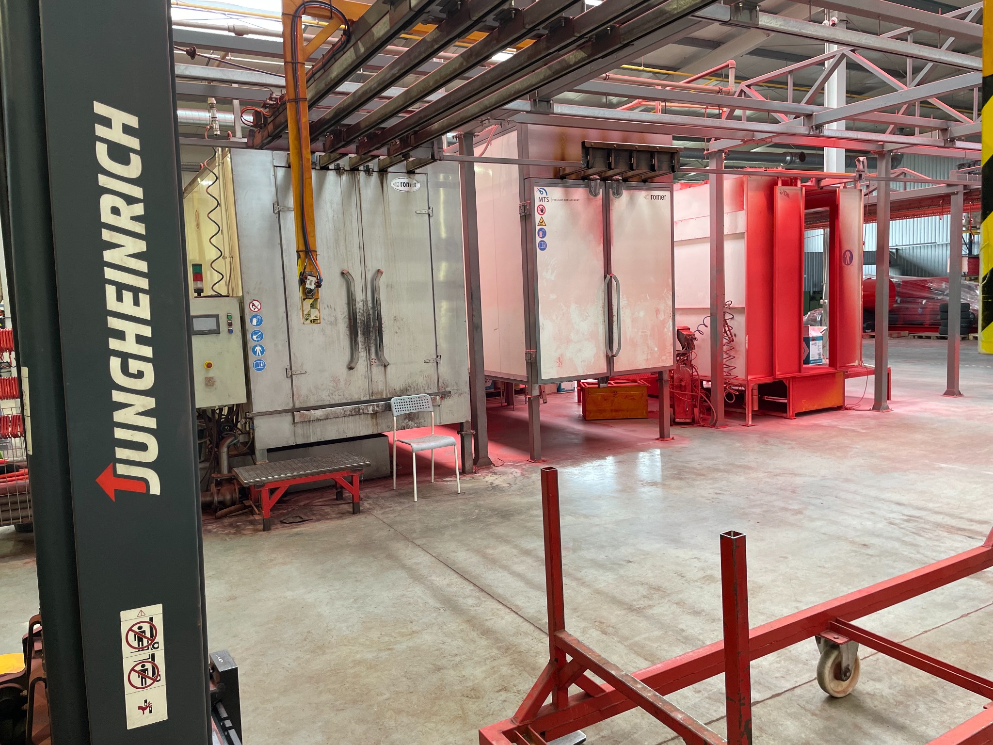 Wnętrze hali produkcyjnej z linią do malowania proszkowego, widoczny wózek widłowy Jungheinrich oraz metalowe konstrukcje do transportu elementów.