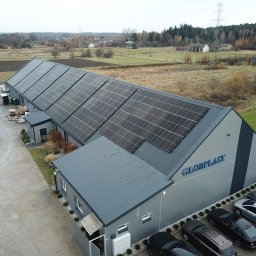 Etikon - Widok z góry na szary budynek firmy Globplast z panelami słonecznymi na dachu, zaparkowanymi samochodami i osobą w czerwonych butach na betonowym placu.