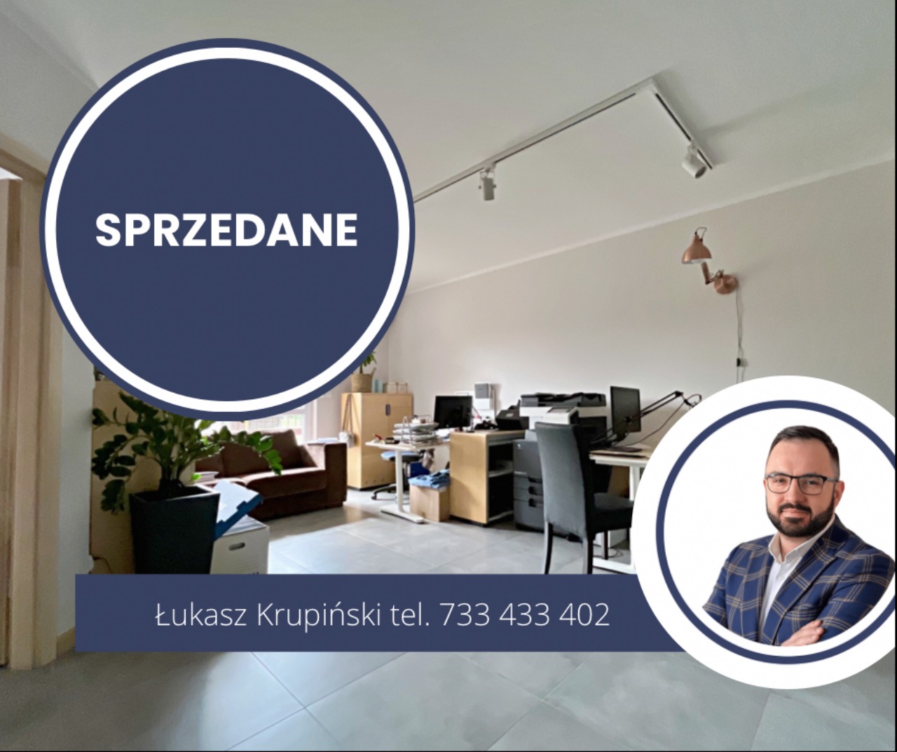 Wnętrze biura z napisem 'Sprzedane' w okręgu, widoczny kontakt do agenta nieruchomości Łukasza Krupińskiego, biurka z komputerami, brązowa sofa, oświetlenie szynowe i lampka ścienna.