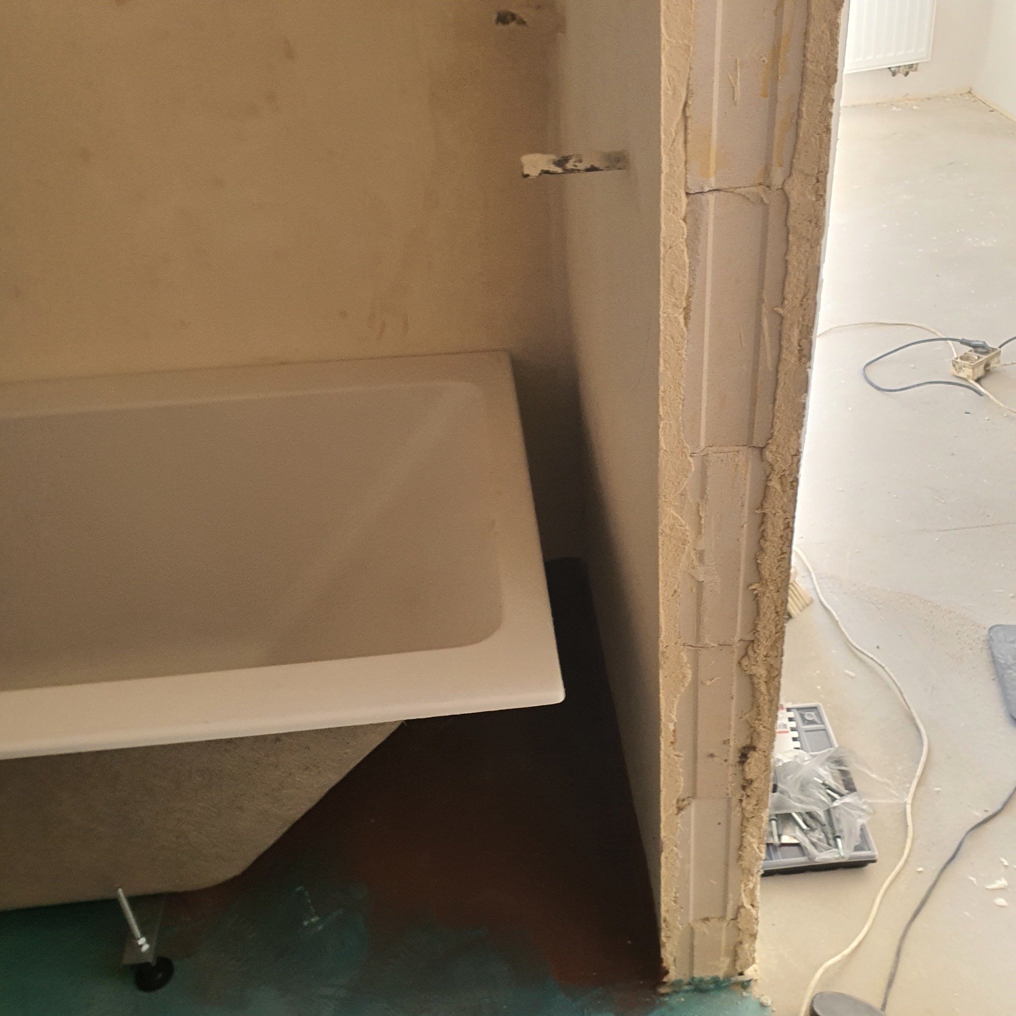 Wanna w trakcie montażu, widoczna surowa ściana łazienki, narzędzia i przewody na podłodze, przygotowania do wykończenia.