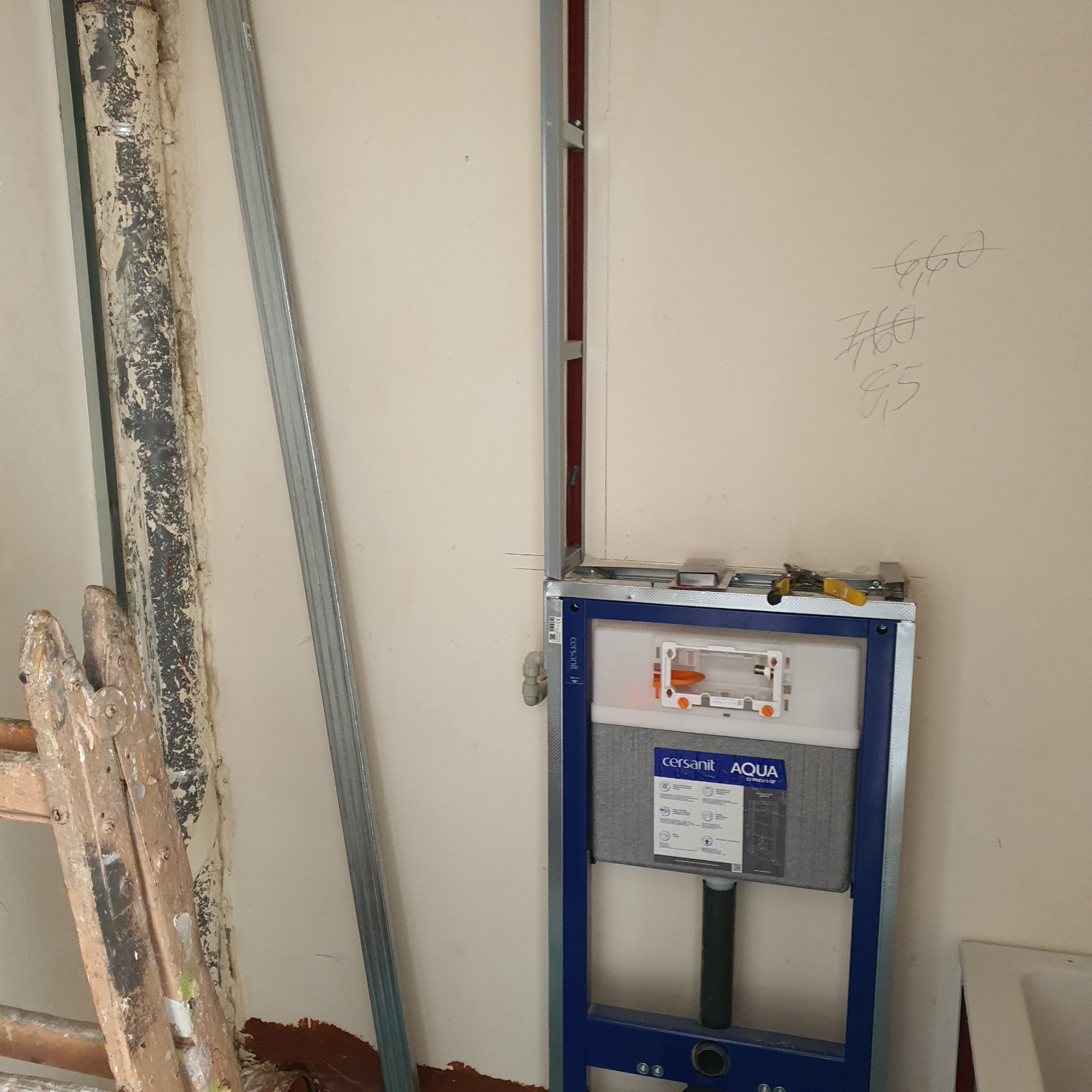 Stelaż podtynkowy WC marki Cersanit Aqua, zamontowany w łazience w trakcie prac remontowych, widoczny z narzędziami na górze i fragmentem drabiny malarskiej w tle.