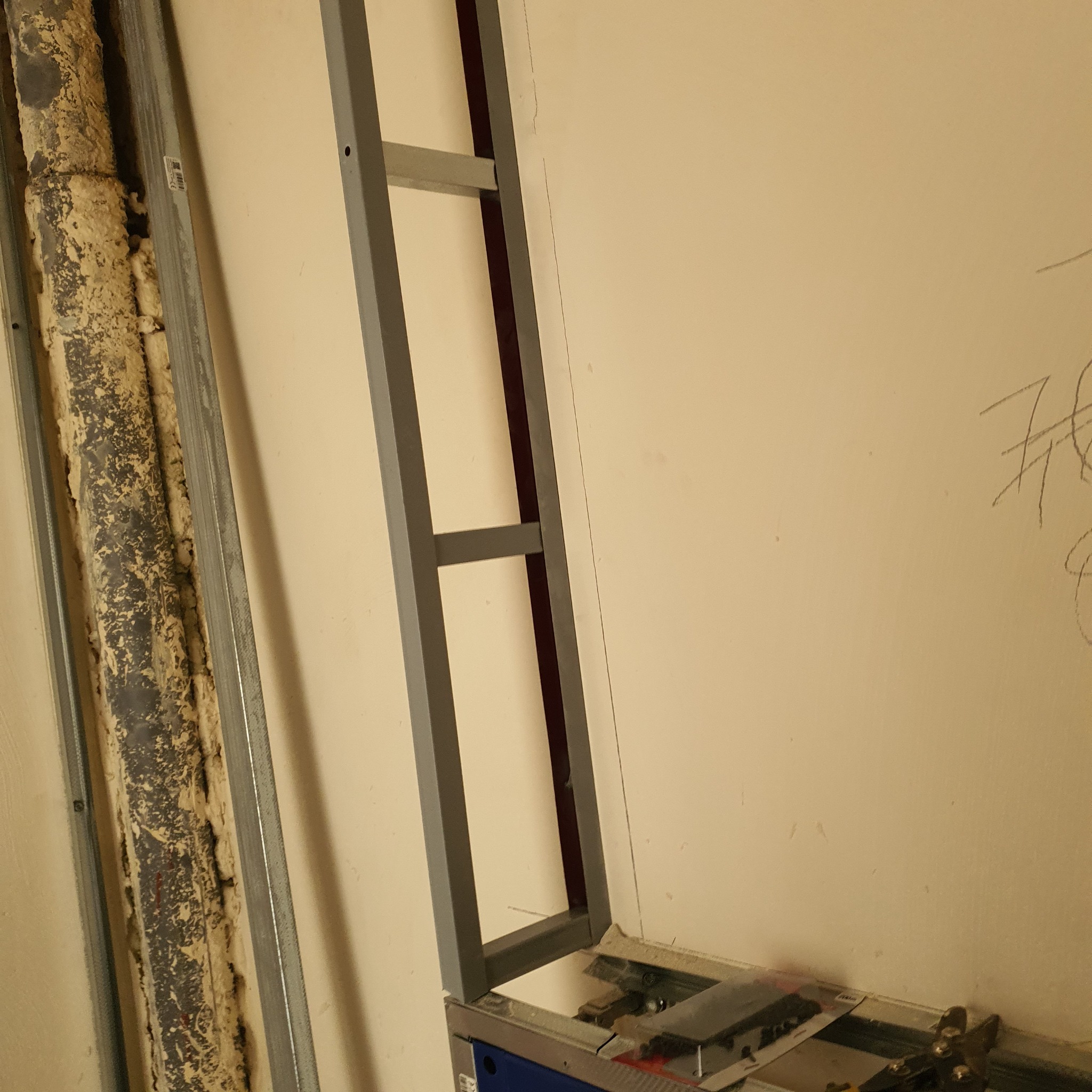 Metalowy stelaż do płyty karton gips, częściowo zamontowany przy ścianie, obok widoczna instalacja zakryta pianką montażową i profilem, na ścianie widoczne ślady ołówka.